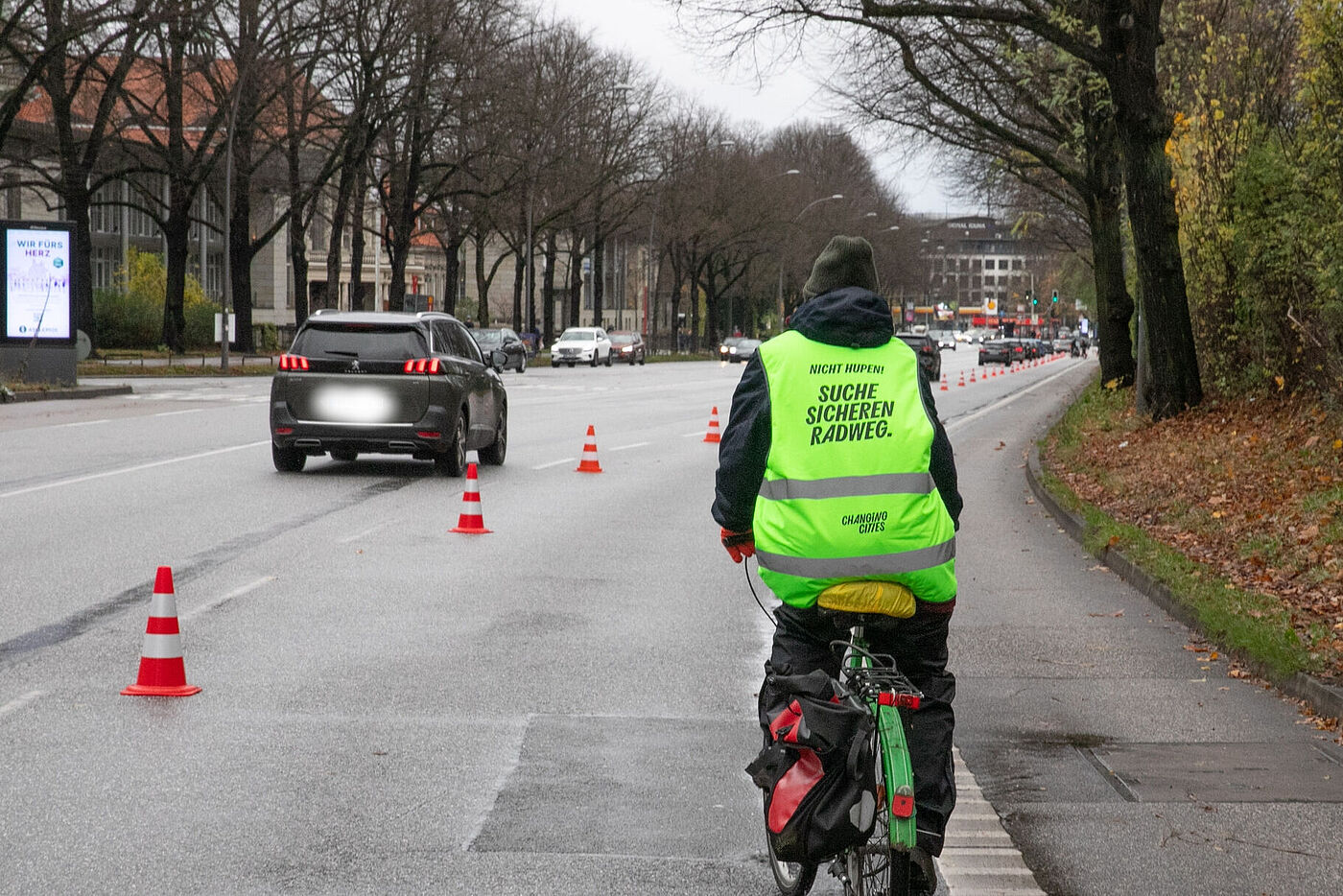 Sicher Radweg gesucht Radfahrende Person mit "Suche sicheren Radweg" auf der Warnweste