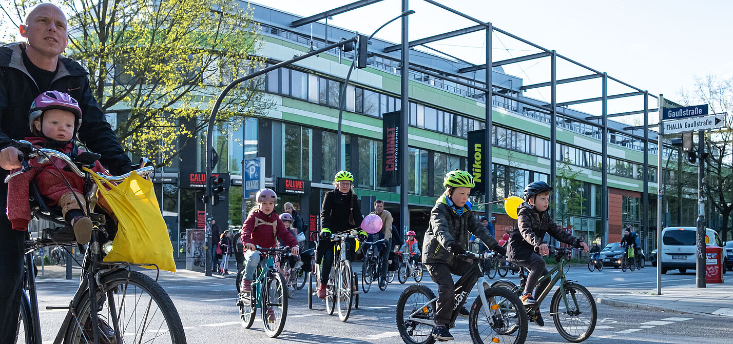 BiciBus in Hamburg Eine Gruppe von Kindern fährt auf ihrer Rädern auf der Straße. Sie werden von Erwachsenen begleitet.